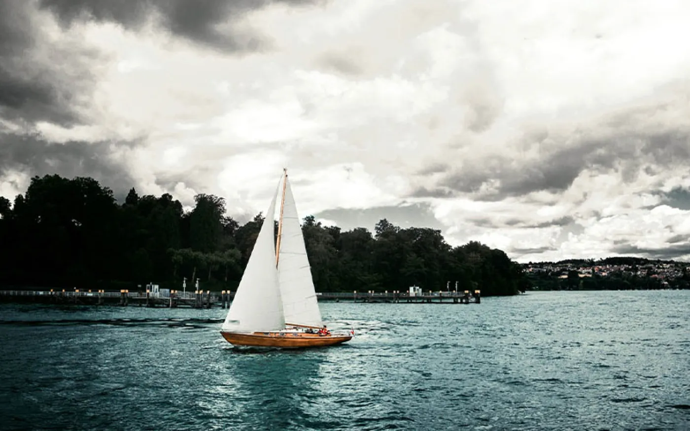 Image of a sailboat sailing on a lake, with cloudy weather above.